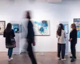 Visitors observe abstract art and a "New York City Rap" poster at a gallery exhibition.