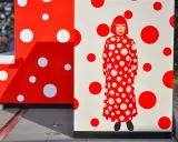 A woman in a red and white polka dot dress stands amidst Yayoi Kusama patterns.
