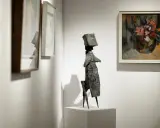 A striking bronze sculpture stands on a pedestal at the London Art Fair, surrounded by framed paintings.