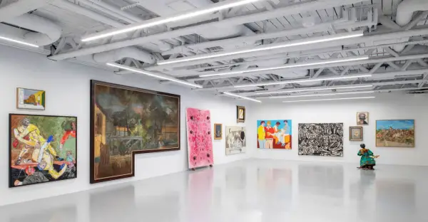 A vibrant art exhibition at Saatchi Yates, featuring diverse paintings and a sculpture, with a striking pink artwork and a figure in a colorful dress.