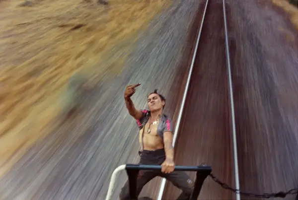 A defiant young man on a train, captured by mike brodie photography, flips the bird against a blur of motion.
