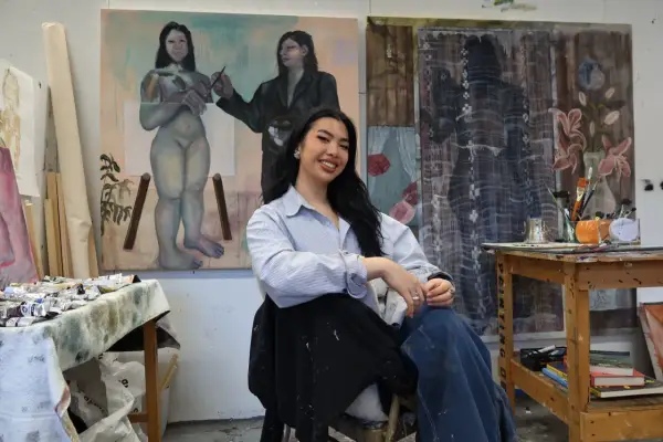 A young woman, one of many talented gen z artists, smiles in her studio, surrounded by her evocative paintings.