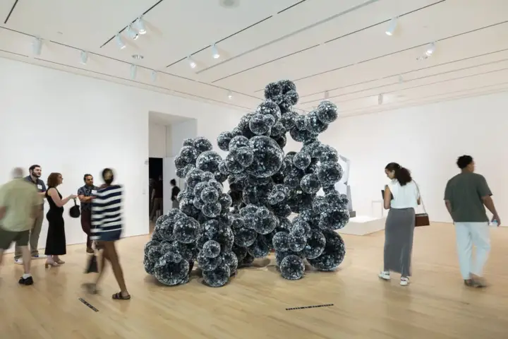 Visitors admire a large, dark, spherical sculpture in a bright gallery space, typical of Indianapolis Museum of Art photos.