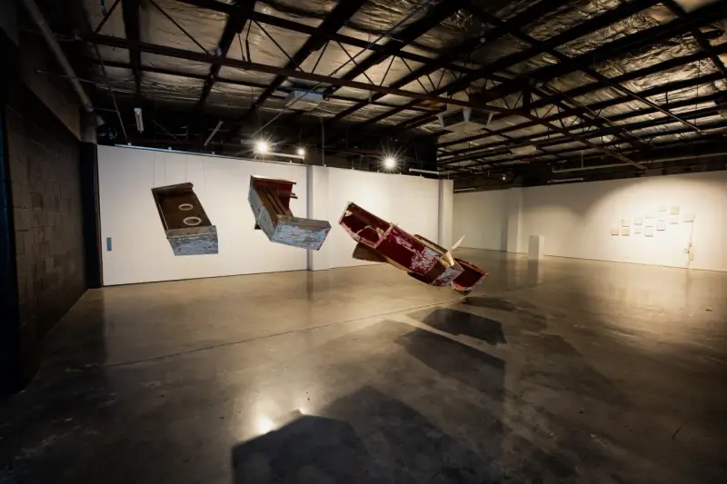 Suspended sculptures of weathered wood and metal hang in the spacious praxis gallery, casting long shadows on the concrete floor.